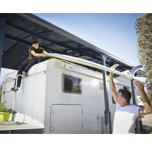 Zwei Personen hieven ein Surfbrett auf ein Wohnmobil mit Markise.
