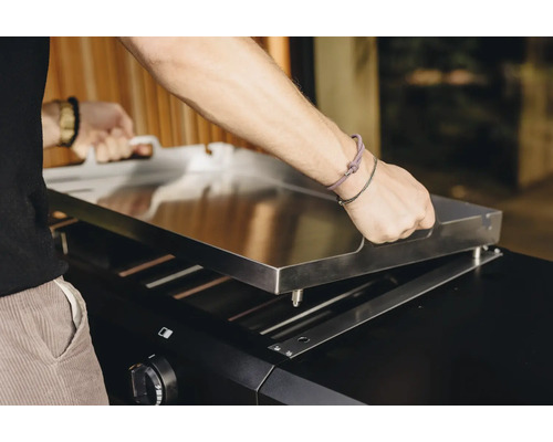Eine Person befestigt eine Grillplatte auf einem Grill.