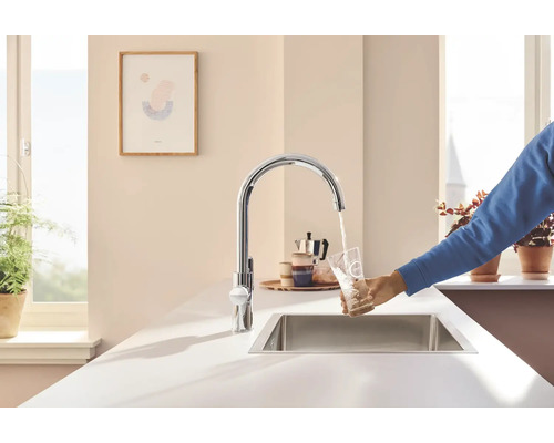 Küchenszene mit Spüle, Armatur und einer Person, die ein Glas Wasser füllt