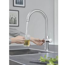 Person lässt Wasser aus einem Wasserhahn in ein Glas laufen, um Tee zuzubereiten.