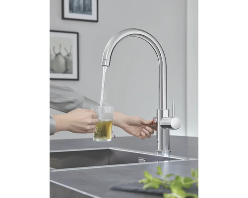 Person lässt Wasser aus einem Wasserhahn in ein Glas laufen, um Tee zuzubereiten.