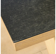 Nahaufnahme einer Tischkante mit dunkler Oberfläche in Steinoptik und einem Rahmen in hellem Holzdekor.