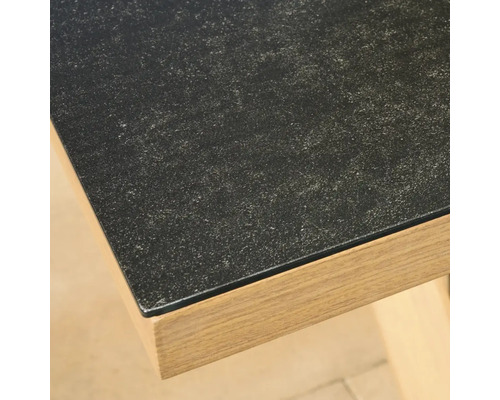 Nahaufnahme einer Tischkante mit dunkler Oberfläche in Steinoptik und einem Rahmen in hellem Holzdekor.