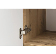 Nahaufnahme eines Topfscharniers aus Metall an einer weißen Schranktür und einem Korpus in Holzoptik.