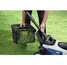 Ein Mann entleert den Fangkorb eines Rasenmähers auf einer Rasenfläche.