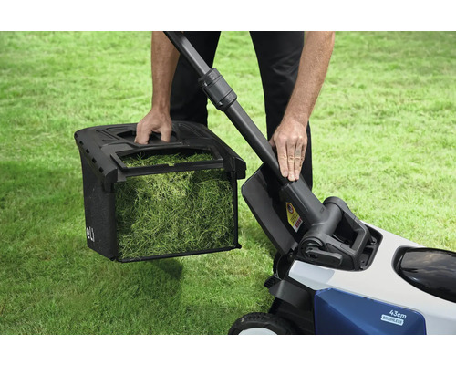 Ein Mann entleert den Fangkorb eines Rasenmähers auf einer Rasenfläche.