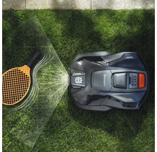 Automatische Rasenmäher bei der Arbeit mit einem Tennisschläger auf dem Rasen