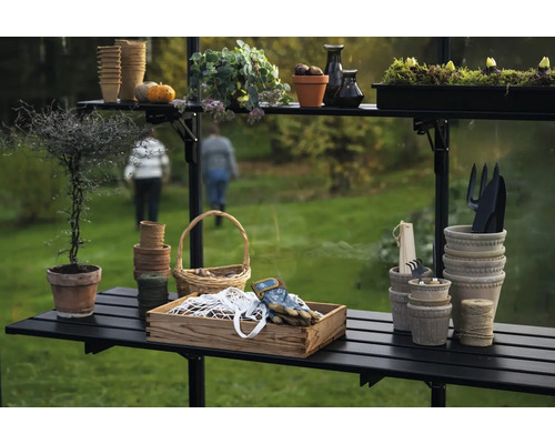 Gartenszene mit Pflanztisch, Töpfen, Werkzeugen und Pflanzen in einem Gewächshaus