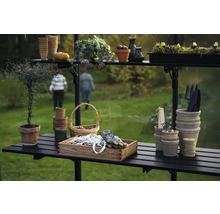 Gartenszene mit Pflanztisch, Töpfen, Werkzeugen und Pflanzen in einem Gewächshaus