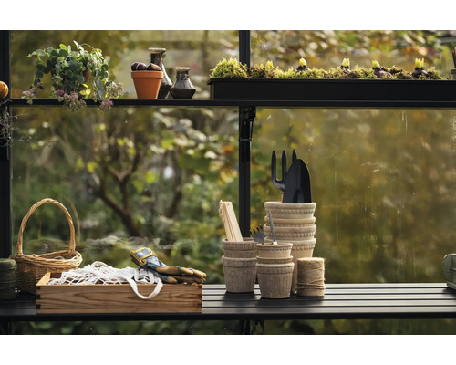 Gartenarbeitsszene mit Pflanzen, Gartengeräten, Töpfen und Accessoires auf einem Tisch im Gewächshaus.