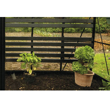 Gewächshaus-Interieur mit Pflanzen in Töpfen vor einem schwarzen Holzgitter