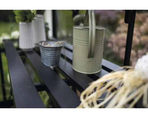 Detailaufnahme eines Gewächshauses mit Regalen, auf denen eine Gießkanne, Töpfe und Vasen stehen.