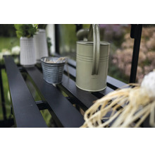 Detailaufnahme eines Gewächshauses mit Regalen, auf denen eine Gießkanne, Töpfe und Vasen stehen.