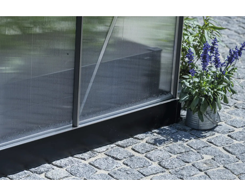 Detailansicht eines Gewächshauses mit Polycarbonatplatten und Aluminiumrahmen, stehend auf Steinpflaster.