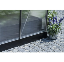 Detailansicht eines Gewächshauses mit Polycarbonatplatten und Aluminiumrahmen, stehend auf Steinpflaster.