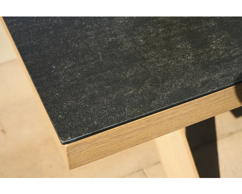 Nahaufnahme einer Tischkante mit dunkler Platte in Steinoptik und Holzgestell.