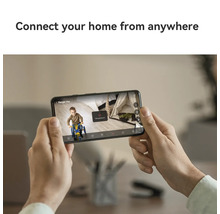Eine Person hält ein Smartphone mit der Anzeige eines Kindes auf einem Dreirad vor einem Zelt.