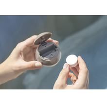 Hände halten eine runde Spenderdose mit geöffnetem Deckel und eine Tablette.