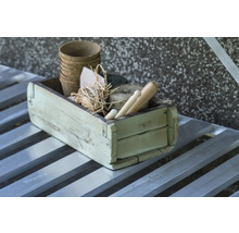 Rustikale Holzkiste mit biologisch abbaubaren Pflanztöpfen, Bindfaden, Bast und Gartenwerkzeugen aus Holz auf einem Metalltisch.