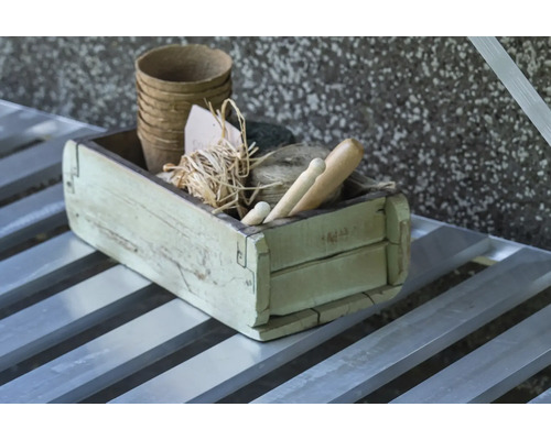 Rustikale Holzkiste mit biologisch abbaubaren Pflanztöpfen, Bindfaden, Bast und Gartenwerkzeugen aus Holz auf einem Metalltisch.
