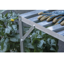 Nahaufnahme eines Aluminium-Pflanztisches mit Gartenhandschuhen und Pflanzen im Hintergrund.
