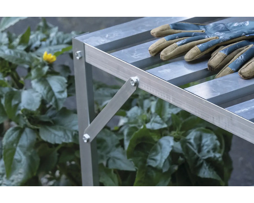 Nahaufnahme eines Aluminium-Pflanztisches mit Gartenhandschuhen und Pflanzen im Hintergrund.