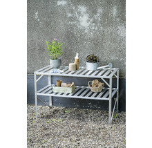 Zweistöckiges Gewächshausregal aus Aluminium mit Pflanzen, Gießkanne und Gartenutensilien auf einer Kiesfläche.