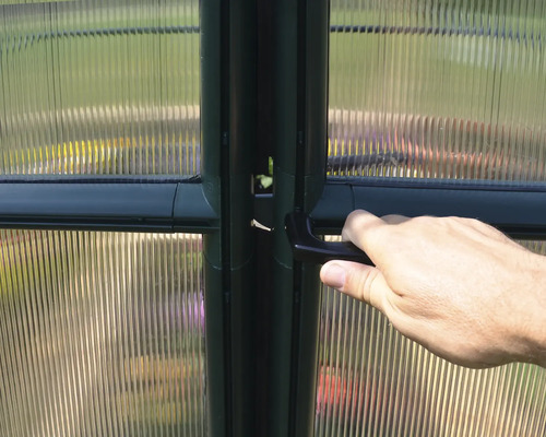Hand am Griff einer Gewächshaustür mit transparenten Polycarbonatstegplatten.