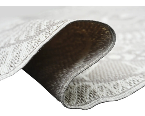 Nahaufnahme eines Flachgewebe-Teppichs mit geometrischem Muster, die Webstruktur und die Rückseite der umgeklappten Ecke zeigt.