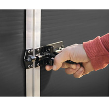 Hand bedient einen schwarzen Metallriegel an einem dunklen Gerätehaus mit silbernem Rahmen.