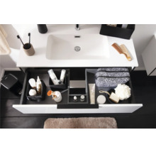 Moderner weißer Waschtisch mit geöffneter Schublade, Schubladen-Organisationssystem mit Toilettenartikeln und hellbraune Badematte.