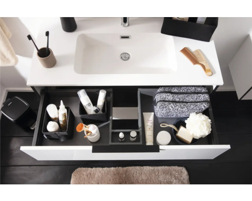 Moderner weißer Waschtisch mit geöffneter Schublade, Schubladen-Organisationssystem mit Toilettenartikeln und hellbraune Badematte.
