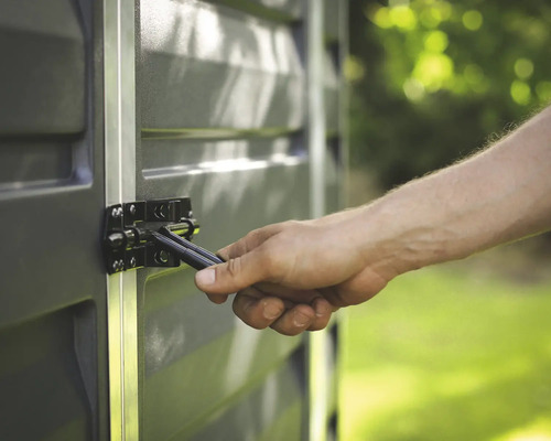 Nahaufnahme einer Hand, die einen schwarzen Metallriegel an einem grauen Gartenhaus mit Aluminiumprofilen betätigt.