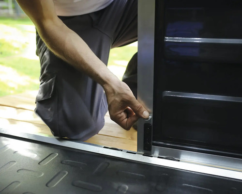 Person montiert einen Riegel an einem Metall-Geräteschrank mit silbernem Rahmen und schwarzen Paneelen.