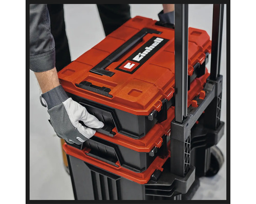 Einhell E-Case System Werkzeugkoffer auf einem Trolley gestapelt, von einer Hand mit Arbeitshandschuh gehalten.