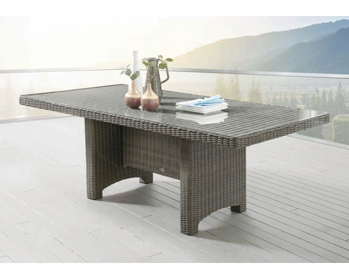 Rechteckiger Gartentisch aus Polyrattan mit Glasplatte auf einer hellen Terrasse mit Aussicht auf Berge.