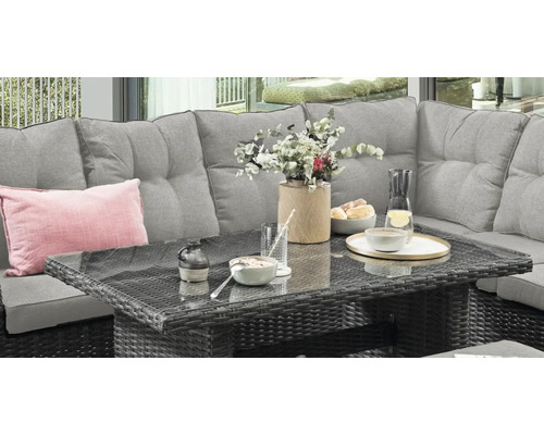 Polyrattan Gartenlounge mit grauem Sofa und Tisch mit Glasplatte, dekoriert mit Geschirr und Blumen auf einer Terrasse.