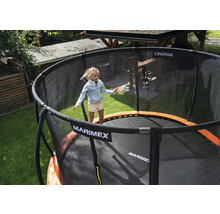 Ein Kind springt auf einem runden Marimex Gartentrampolin mit schwarzem Sicherheitsnetz und orangefarbenem Randschutz in einem Garten.