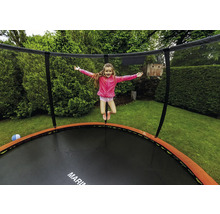 Ein Kind springt auf einem runden Gartentrampolin mit Sicherheitsnetz und orangefarbenem Randschutz in einem grünen Garten.