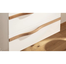 Nahaufnahme eines Badezimmerschranks mit weißen Schubladenfronten und geschwungenen Griffen aus Holz.