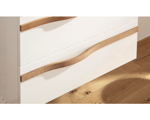Nahaufnahme eines Badezimmerschranks mit weißen Schubladenfronten und geschwungenen Griffen aus Holz.