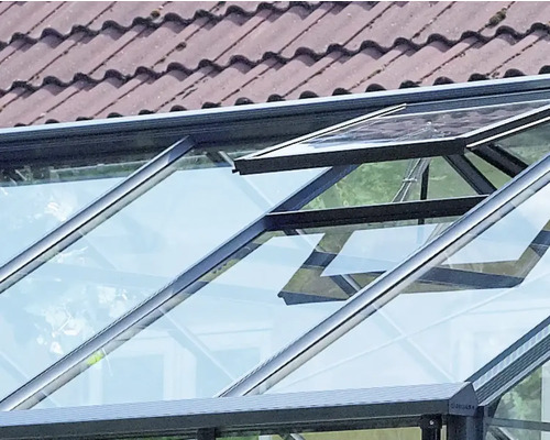 Gewächshausdach mit einem geöffneten Dachfenster aus Glas und dunklem Metallrahmen.