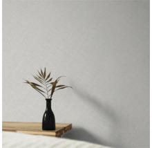 Vliestapete mit feiner Leinenstruktur an einer Wand hinter einer Vase mit getrocknetem Blatt auf einem Holztisch.