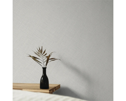 Vliestapete mit feiner Leinenstruktur an einer Wand hinter einer Vase mit getrocknetem Blatt auf einem Holztisch.