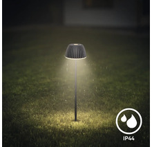 Moderne LED Gartenleuchte mit geripptem Schirm leuchtet nachts auf einem Rasen, spritzwassergeschützt gemäß Schutzart IP44.