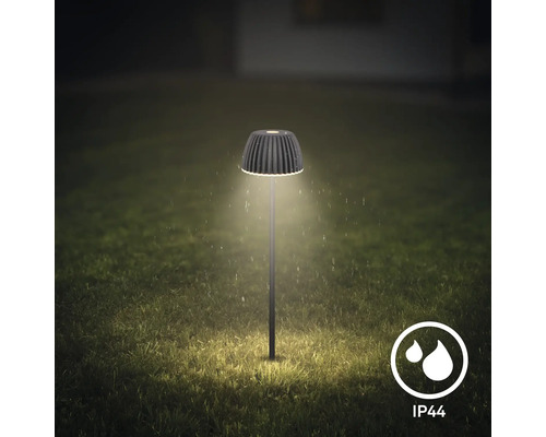 Moderne LED Gartenleuchte mit geripptem Schirm leuchtet nachts auf einem Rasen, spritzwassergeschützt gemäß Schutzart IP44.