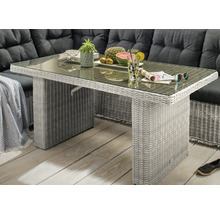 Gartentisch aus Polyrattan mit Glasplatte vor einer Lounge-Ecke mit dunklen Polstern auf einer Terrasse.
