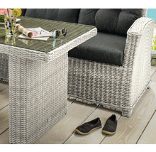 Gartenmöbel Set aus hellem Polyrattan Geflecht mit Glastisch und Lounge Sessel mit dunklen Kissen auf einer Holzterrasse.