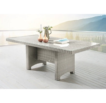 Rechteckiger Gartentisch aus Polyrattan-Geflecht mit Glasplatte auf einer hellen Terrasse vor einer Gebirgskulisse.