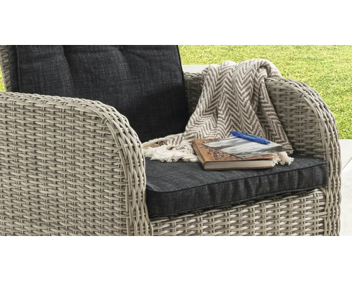 Gartensessel aus Kunststoffgeflecht mit Polsterauflagen, einer Decke mit Fischgrätmuster, einem Notizbuch, einem Foto und einem Stift.